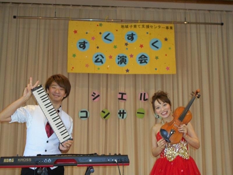 鍵盤ハーモニカを持ちピースサインをしている男性とバイオリンを持ち笑顔で立っている女性の写真
