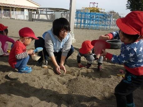 保育士姿のお父さんが砂場で子供たちと一緒に遊んでいる写真