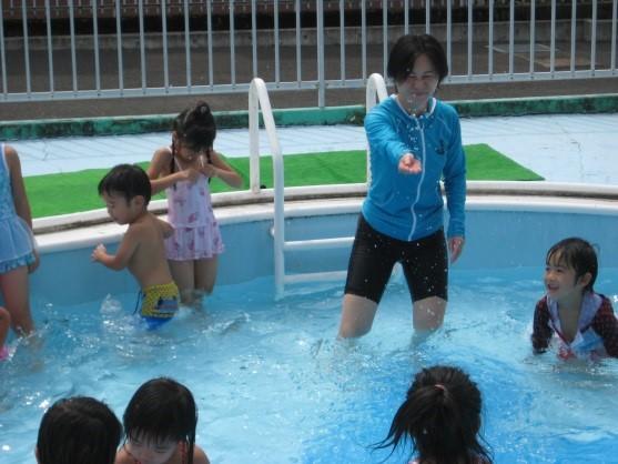 保育園内のプールで一日保育士体験のお母さんと7名の園児たちが水遊びをしている写真
