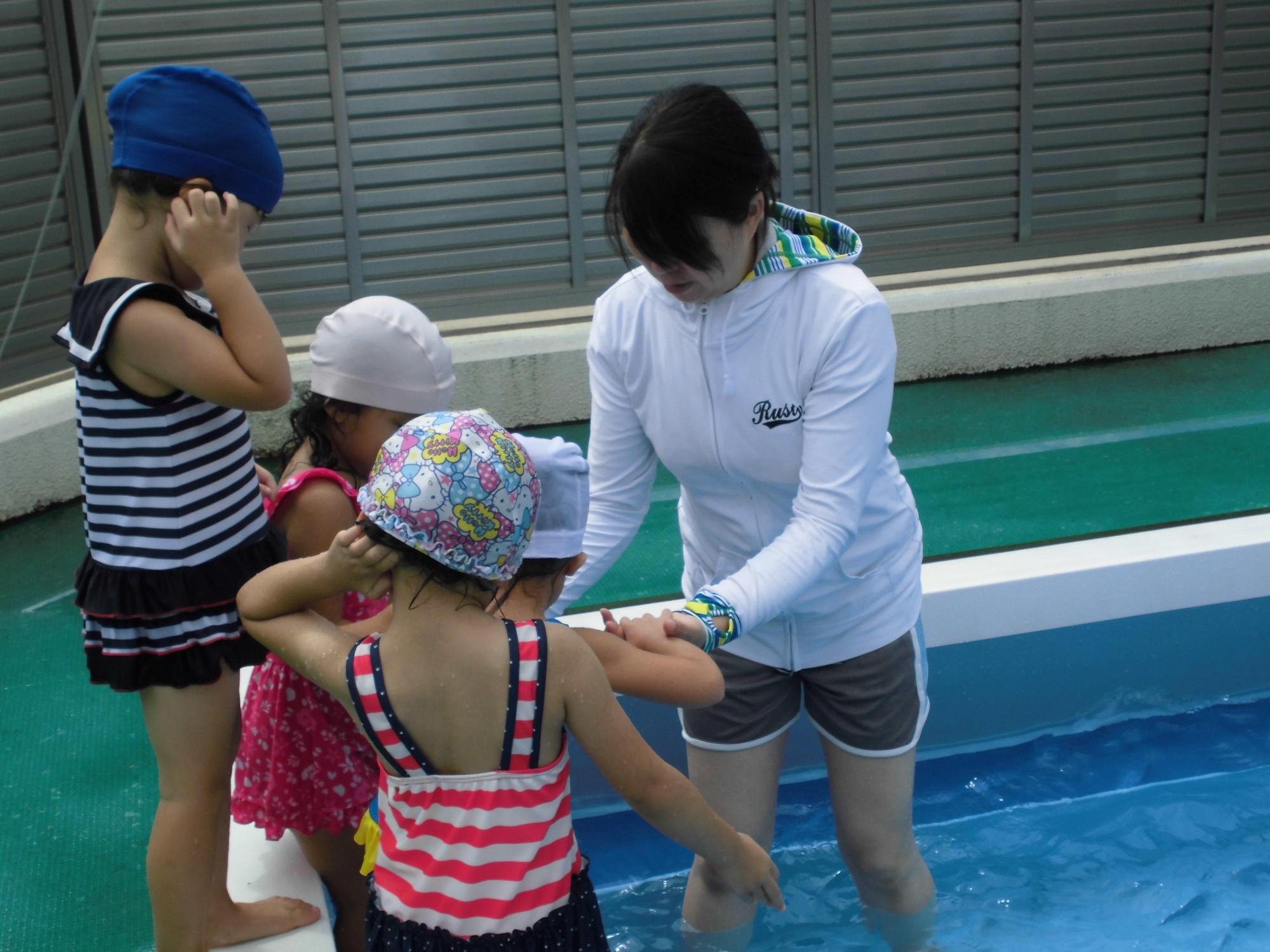 保育園でプール遊びをしている一日保育士体験のお母さんと水着の園児たちの写真