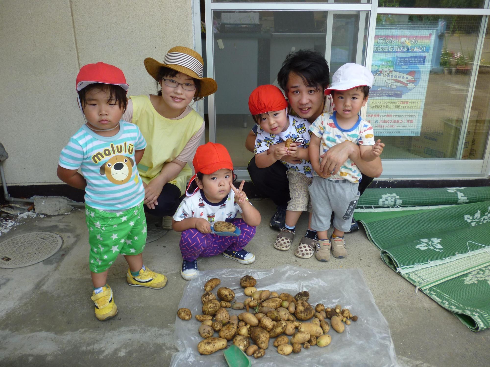 一日保育士体験のお母さんと保育士の先生と2歳児クラスの園児4人が収穫したじゃがいもと一緒に写っている写真