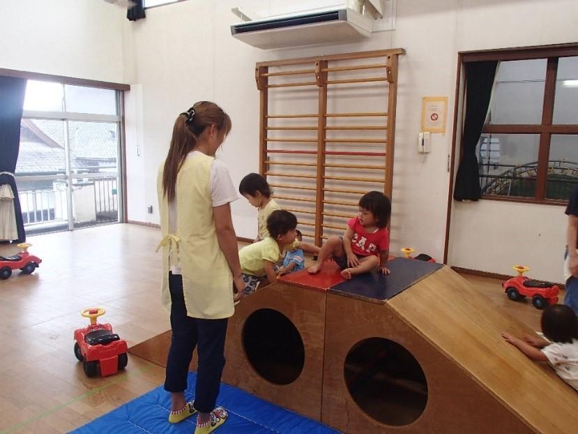 室内にある木製の滑り台で遊んでいる子供たちとそれを見守る保護者の写真