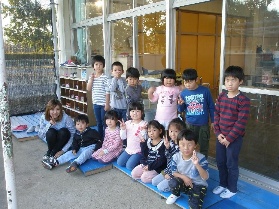 保育園の教室の出入り口の前で一日保育士体験のお母さんと園児たちがピースサインをして撮った集合写真