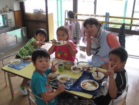 一日保育士体験のお母さんと4人の園児が給食を食べながらピースサインをしている写真