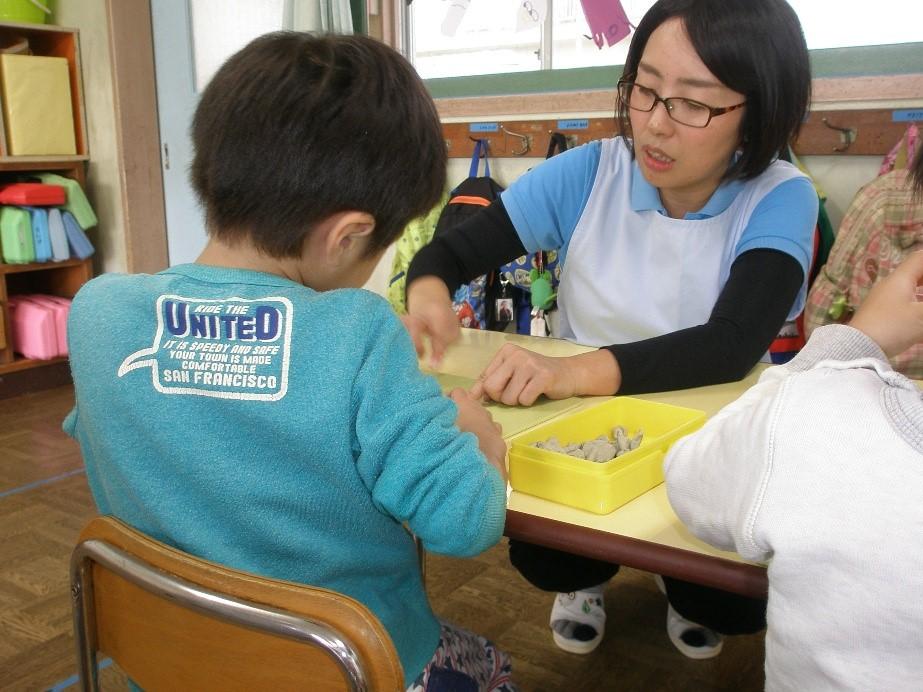 保育園の教室で机に向かって粘土遊びをしている男児と一日保育士体験のお母さんの写真