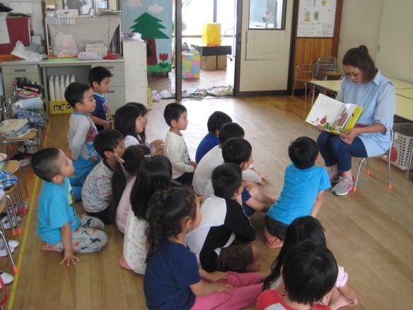 青いエプロンをつけたお母さんが子供たちに絵本の読み聞かせをしている写真