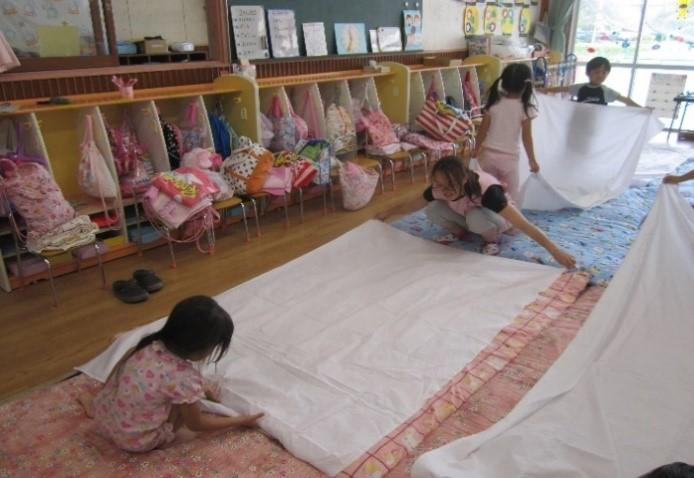 お昼寝の準備でお布団を敷いている保護者と園児たちの写真