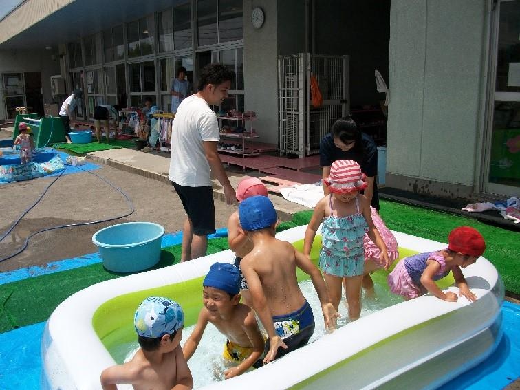 ビニールプールに水着を着て水泳帽を被って楽しそうに遊んでいる子供たちの写真
