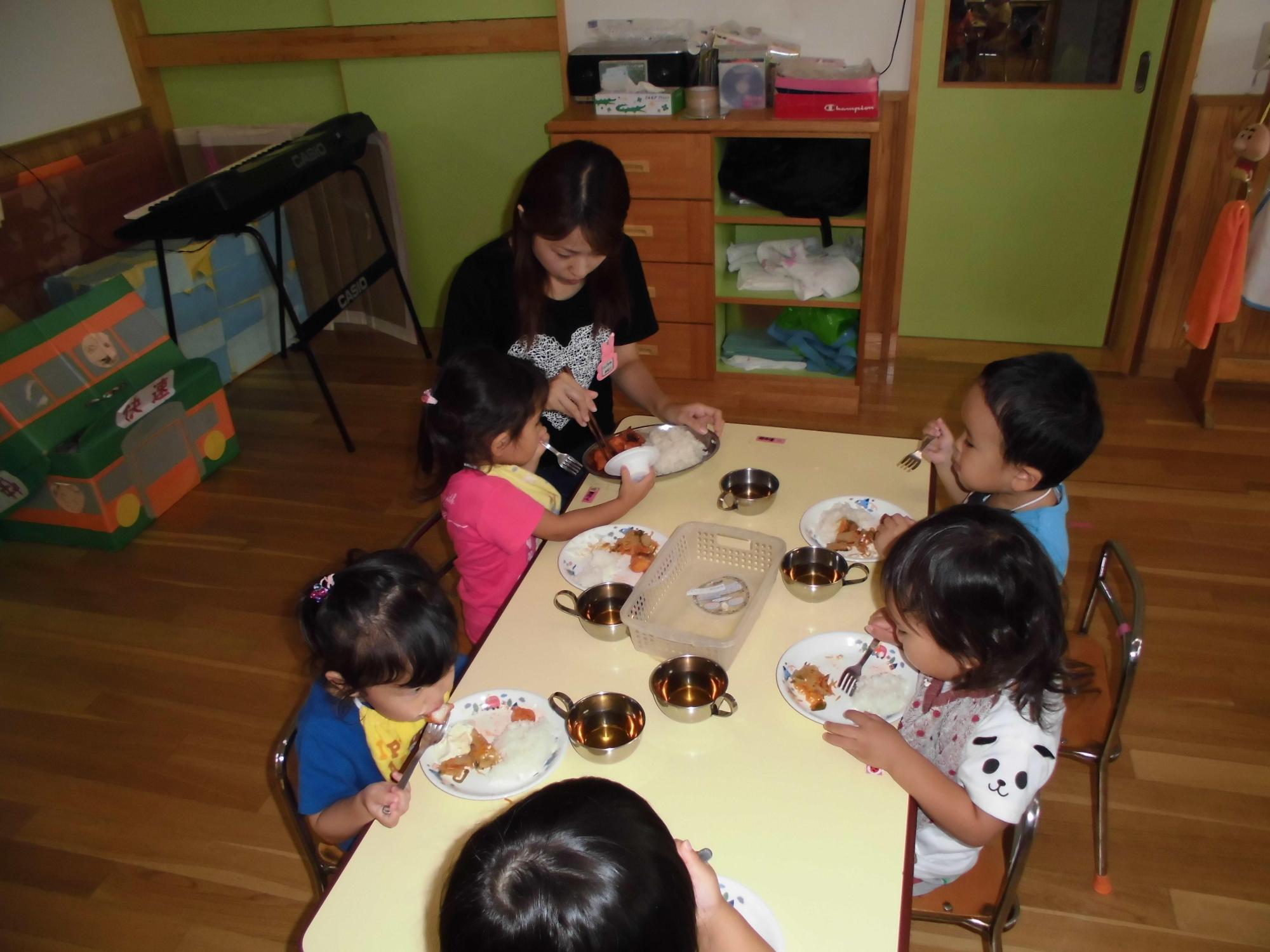 給食の時間フォークを使って食事をしている園児たちと同じテーブルで給食を食べている一日保育士体験のお母さんの写真