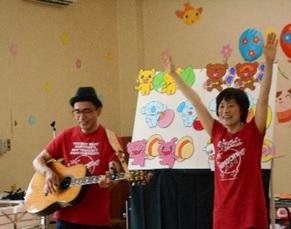 左側にギターを演奏している男性と右側に両手を挙げている女性講師の写真