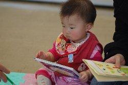 ピンク色の服を着た赤ちゃんに読み聞かせをしている写真