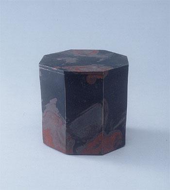 黒地に赤色などが混在し彩色された八角形の筒状の箱の作品の写真
