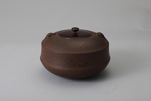 文様を浮き上がらせることによって描き、海亀の鐶付がつけられたこげ茶色の茶の湯釜の作品の写真