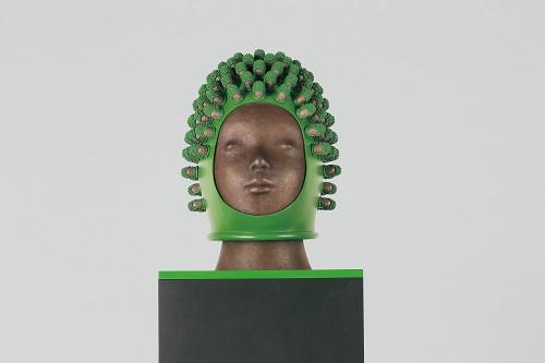 首から上の銅像が頭部に緑色のマスクをかぶっておりそのマスクにその銅像の頭部のミニチュアが無数についている作品の写真