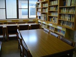 机と椅子があり壁の本棚には本が沢山置いてある図書室の写真