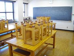 前方に黒板と木製の机の上に椅子が並べられている工芸室の写真