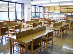 壁際の本棚に図書の本が並んでおり中央に机といすが並べられている図書室の写真