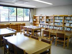 壁にたくさんの図書の本がならんでおり机といすがある図書室の写真