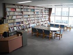 壁に本棚が設置してあり、その本棚に本がぎっしりと並んでいて、その横には机と椅子が置いてある図書室の写真