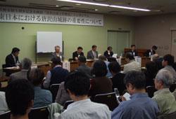 10月31日開催のシンポジウム会場にて前方に座っている専門家の方たち7名と客席にいる参加者たちの写真