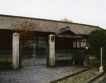 入り口の門の両端に白い柱が立っており一階建ての旧三好小学校校舎の外観の写真