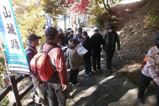 唐沢山城跡の山道の途中登り旗が道のわきに立てられておりボランティアガイドとツアー参加者が資料を眺めている写真