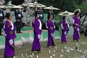 牧歌舞伎の演技中：紫色の衣装にかつらをかぶり番傘を持っている5人が並んでいる写真