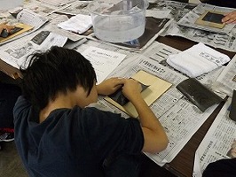 テーブルに新聞紙を広げ石灰岩を磨いている男の子の後ろからの写真