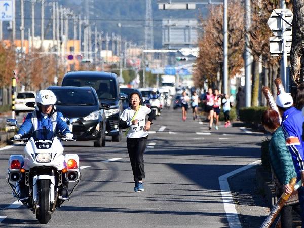 沿道には応援者、白バイに先導され走る女子選手の写真