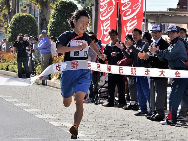 沿道で拍手を送る応援者とゴールのテープを切る女子選手の写真