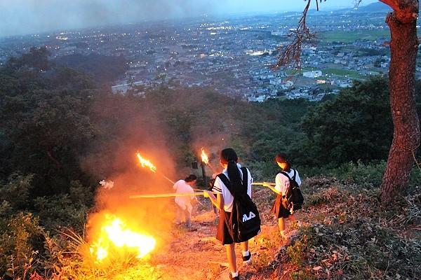 女子学生が火のついたたいまつを持って山を下りている写真
