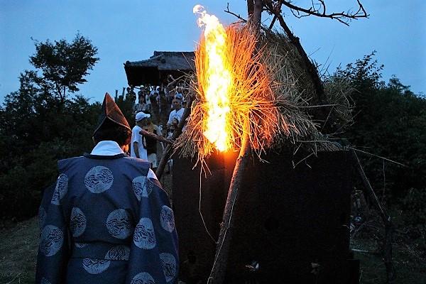 参加者が見守る中神主が小麦わらへ火をつけている様子の写真