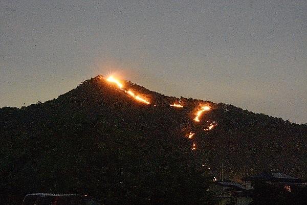 山頂から火を持つ人でできた光の道が見える写真