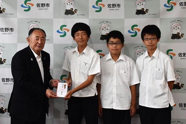 男子中学生3人のうち代表者1名が佐野市長からお祝いを受け取っている写真