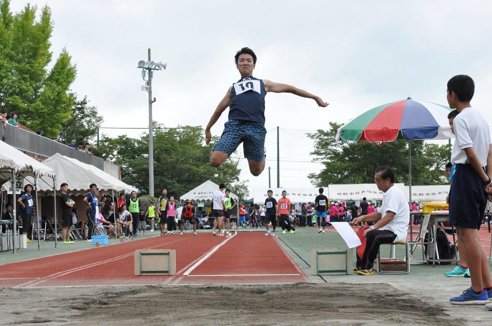 走り幅跳びの競技で砂場を飛んでいる男性の写真