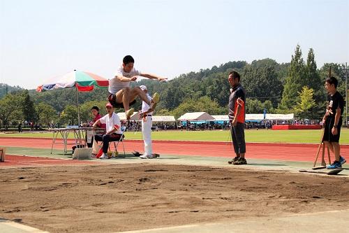 走り幅跳び男子の部の競技で両手を挙げて高く飛んでいる写真