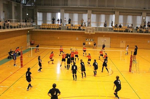 バレーボールの女子の試合で高く上がったボールをアタックしたボールをブロックしようとしている写真