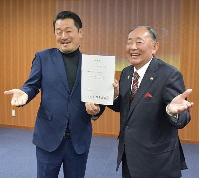 佐野市長とお笑い芸人のテルさんが任命書を片手で一緒に持ち笑顔で記念撮影をしている写真