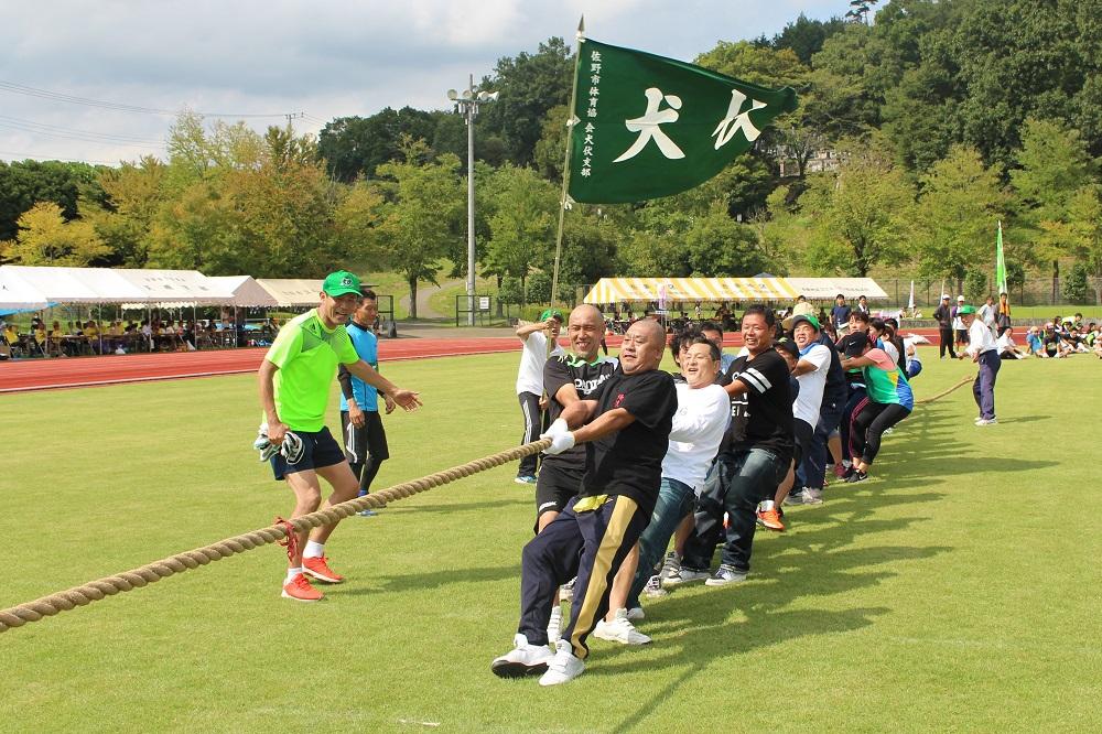 綱引きをしている選手と犬伏と書かれた旗を振りながら応援している方の写真